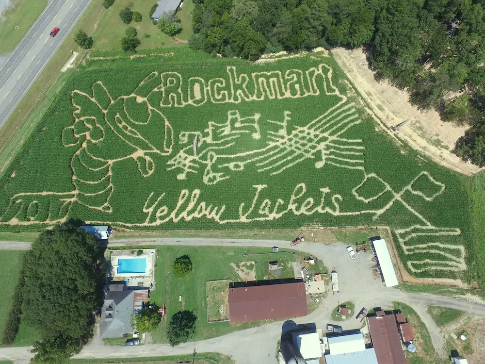 Aerial view of a corn maze depicting a musical theme with the word 'Rockmart' and 'Yellow Jackets' along with a hornet mascot and music notes.